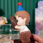 HACIPUPU-Whispers-of-My-World Toy figure of a character with a blue hat holding a chocolate donut, blurred background