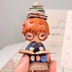Hirono-Le-Petit-Prince Figurine of a character with glasses and books, held by a hand against a light background.
