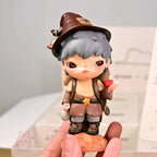Hirono-Le-Petit-Prince Small figurine of a character with a hat and backpack held by a hand against a blurred background