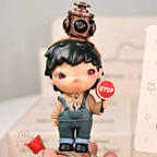 Hirono-Le-Petit-Prince Toy figure of a character with a stop sign and a camera on their head, held by a hand.