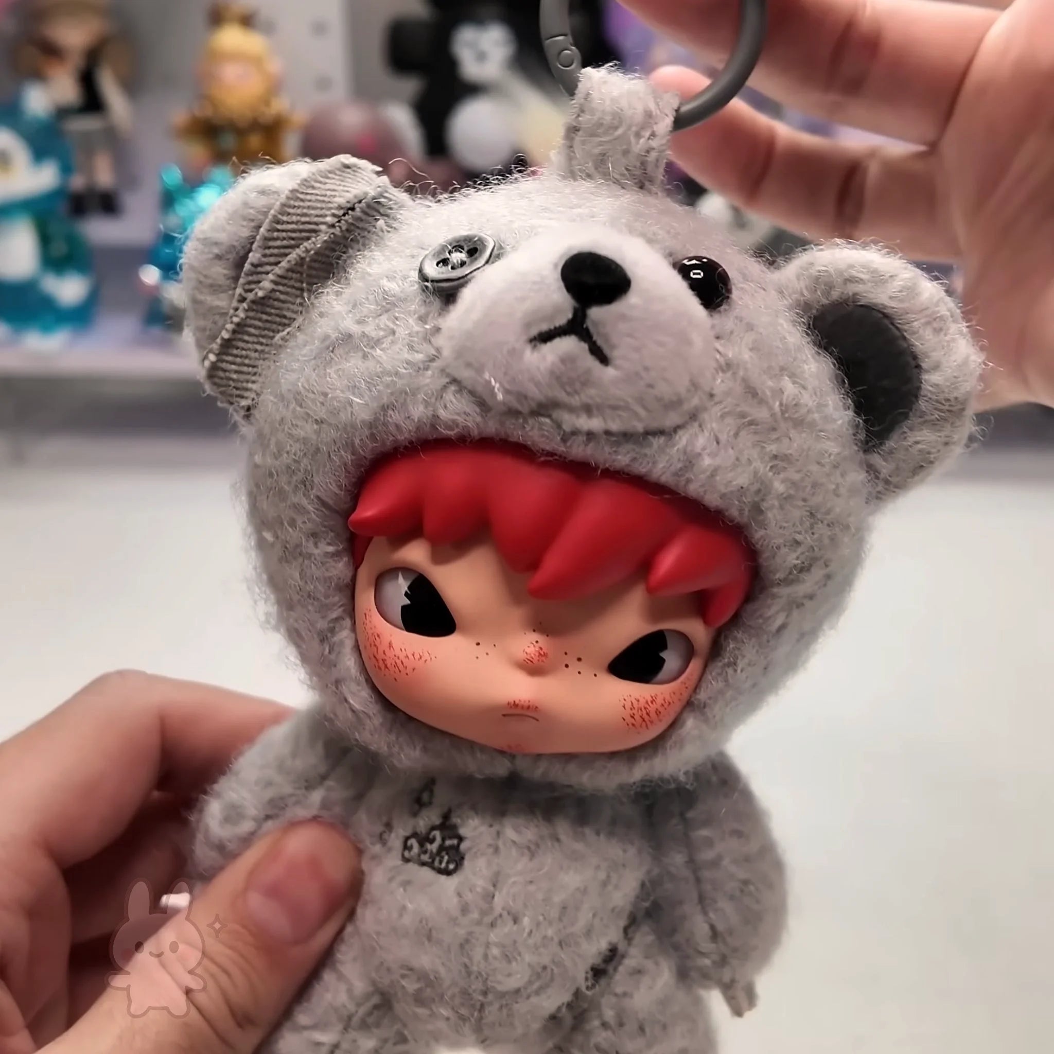Hirono Road Journal Series Plush Doll Plush keychain with a character wearing a gray bear costume on a blurred background