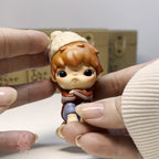 Hirono The Other One Small figurine of a character with a beanie held between two hands against a neutral background
