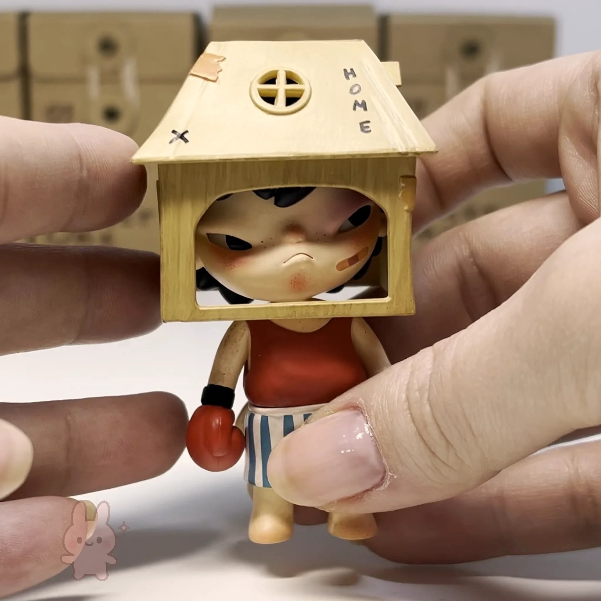 Hirono The Other One Small figurine with a house-shaped head held between fingers