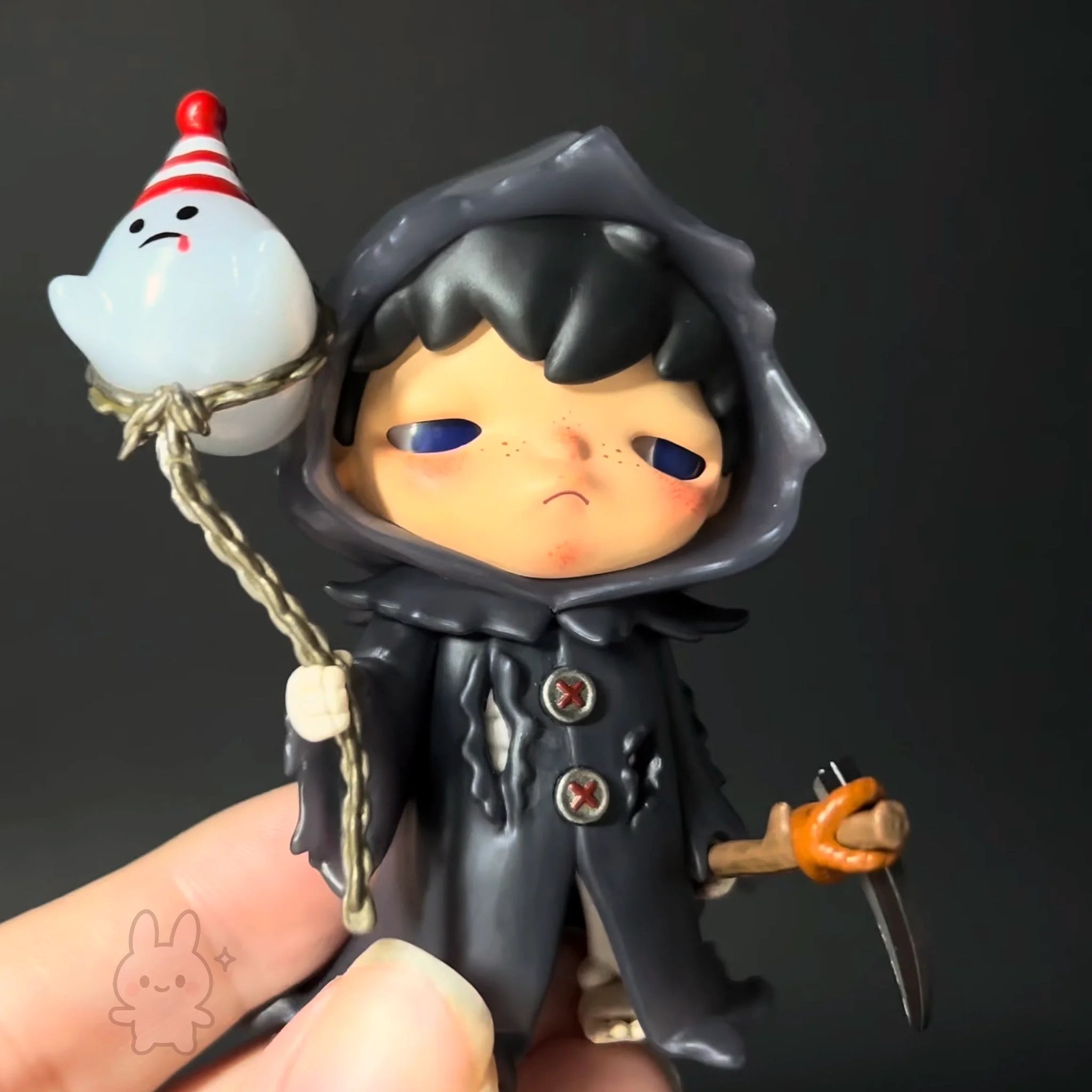 Hirono-monsters-carnival Figurine of a character in a black hooded outfit holding a small white ghost-like figure on a string.