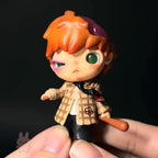 Hirono-monsters-carnival Small figurine of a character with orange hair and plaid coat held by a hand against a black background