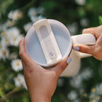 Person holding a White Stanley against a blurred natural background with flowers.