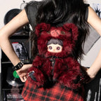 Person holding a red Maymei Rebel Doll plush toy with a character design, wearing a plaid skirt.