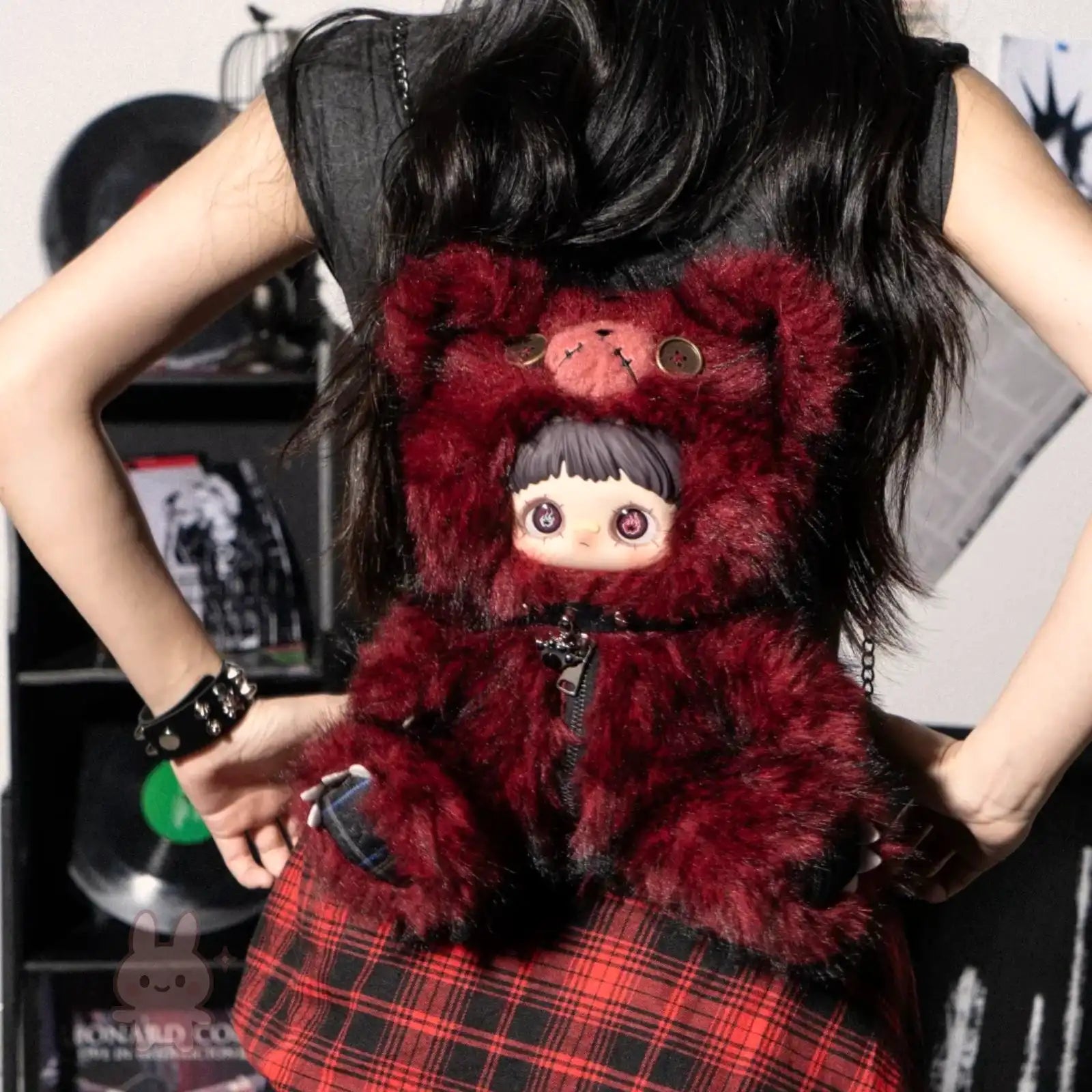 Person holding a red Maymei Rebel Doll plush toy with a character design, wearing a plaid skirt.
