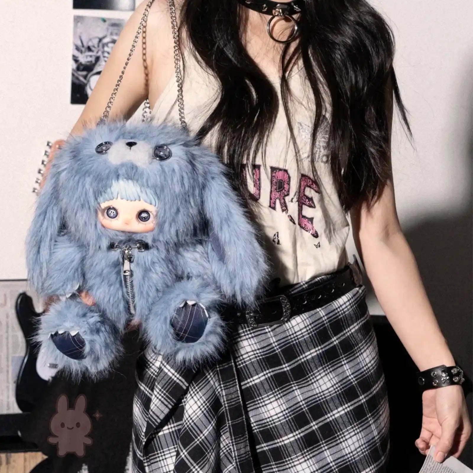 Person holding a blue fluffy Maymei Rebel Doll bag with a character design, wearing a plaid skirt and graphic t-shirt.