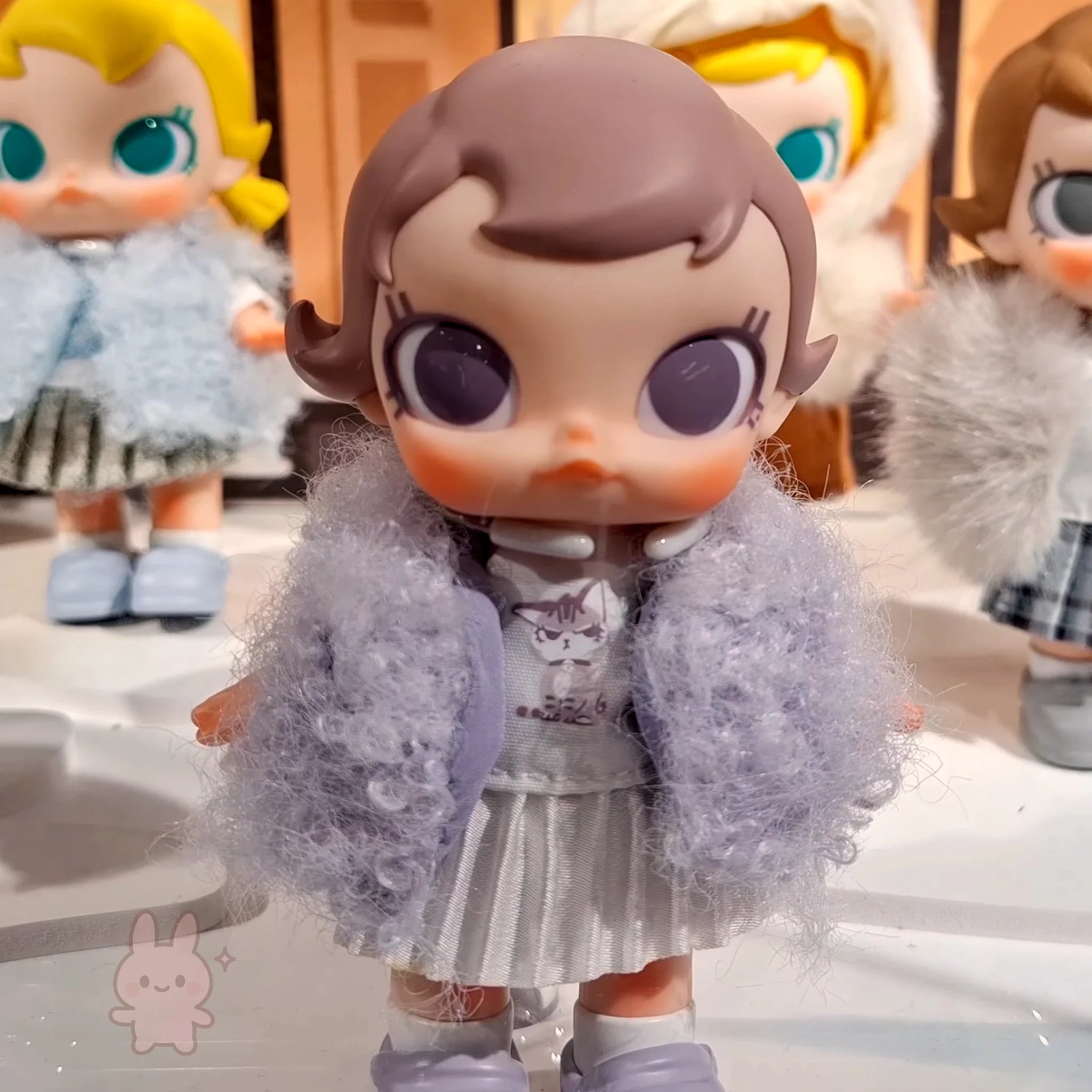 Baby Molly - Winter Fit Check Toy figure with a fluffy gray coat and checkered skirt, standing on a reflective surface.