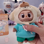 Labubu THE MONSTERS Sanrio Toy figure in a hooded outfit held by a hand with a card in the background