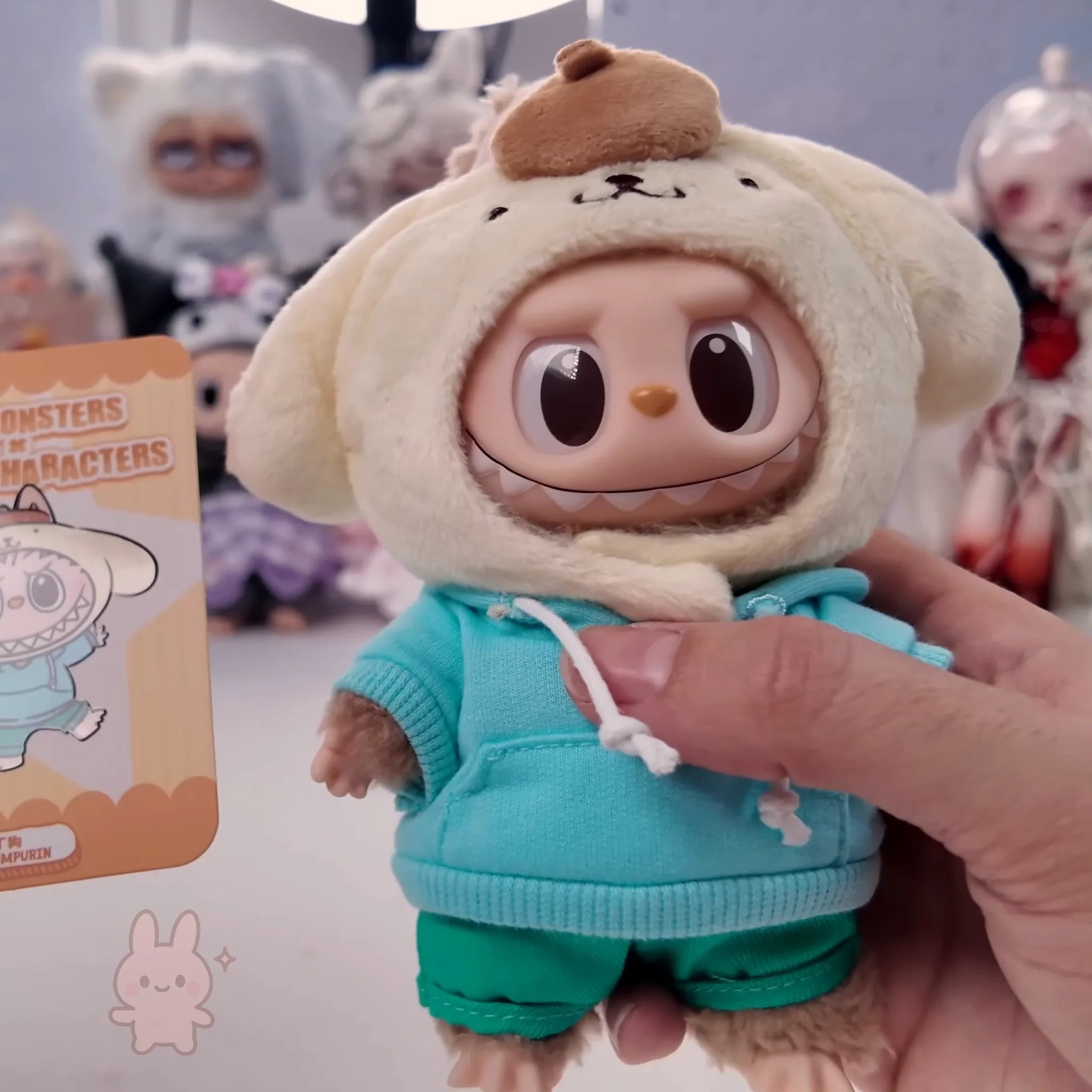 Labubu THE MONSTERS Sanrio Toy figure in a hooded outfit held by a hand with a card in the background