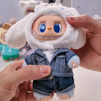 Labubu THE MONSTERS Sanrio Small doll with a denim outfit and white hat held by a hand against a blurred background