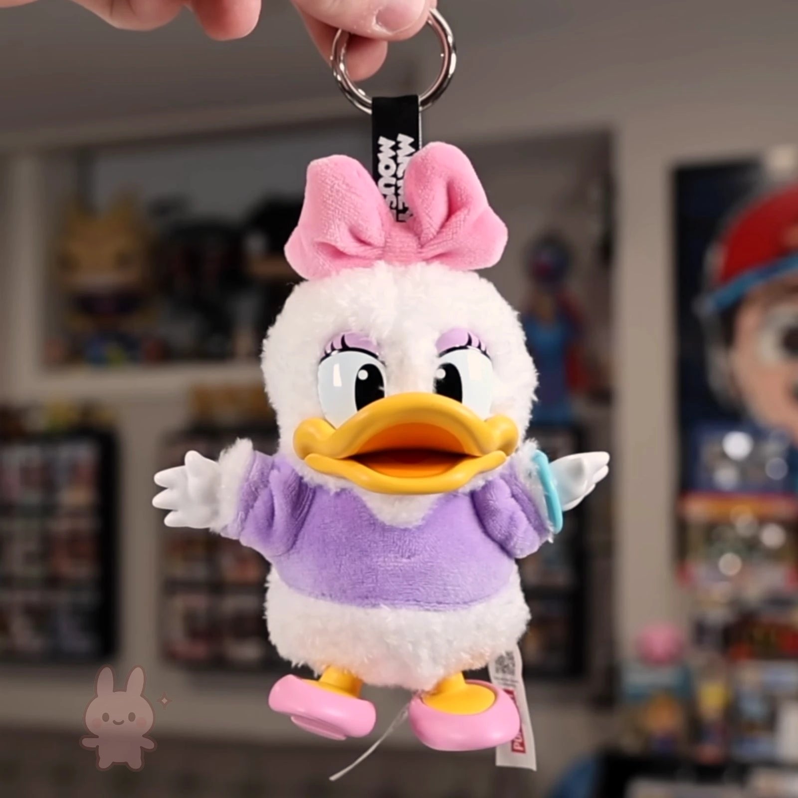 Plush keychain of a cartoon character with a pink bow in a store setting