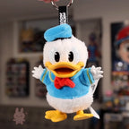 Plush keychain of a cartoon character with a blue hat and sweater, held against a blurred background.