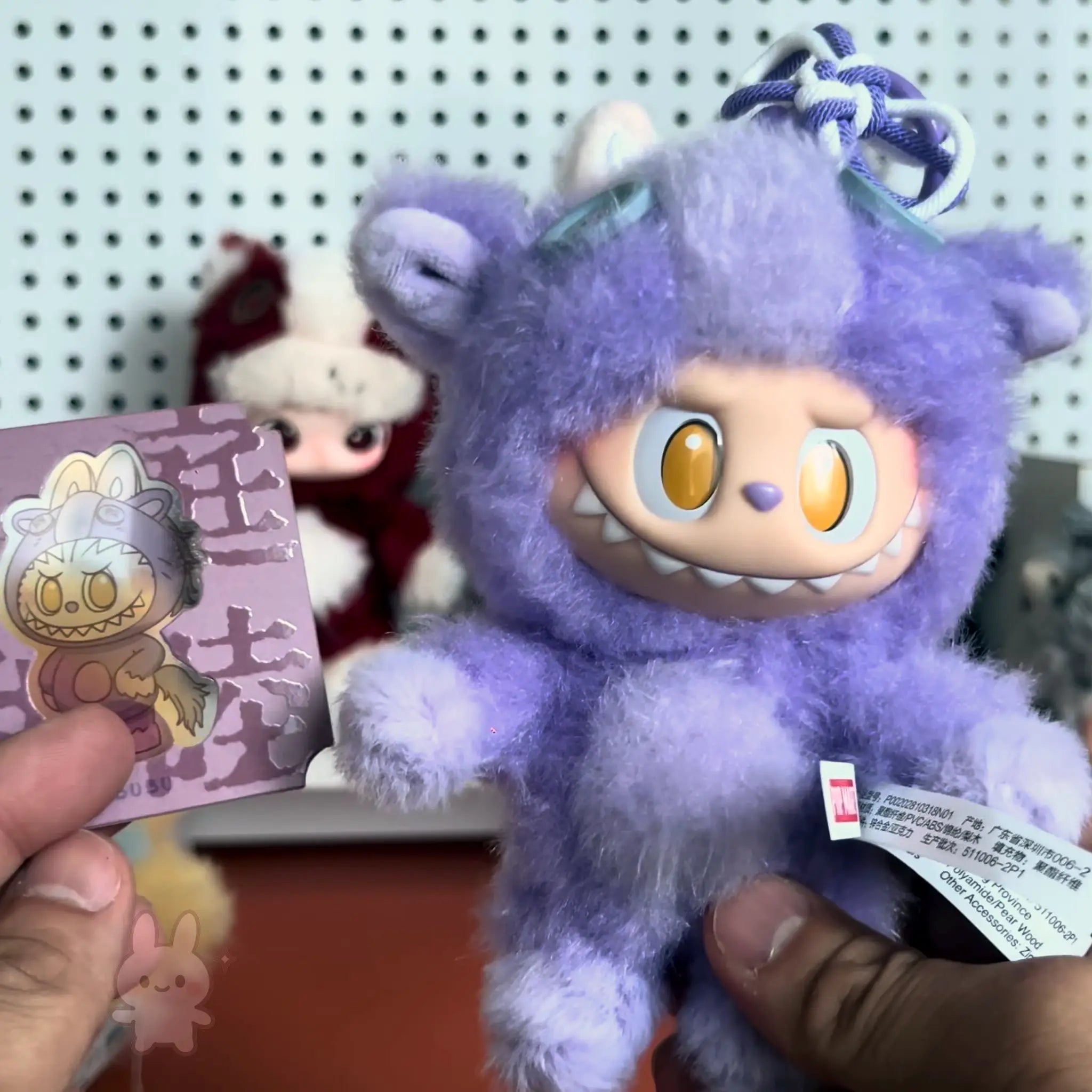 Pop-Mart-Have-a-good-run Purple plush toy with a card featuring a similar design, held against a blurred background.