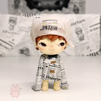 Pop Mart Hirono Little Mischief Toy figure wearing a newspaper outfit with a white cap on a light background