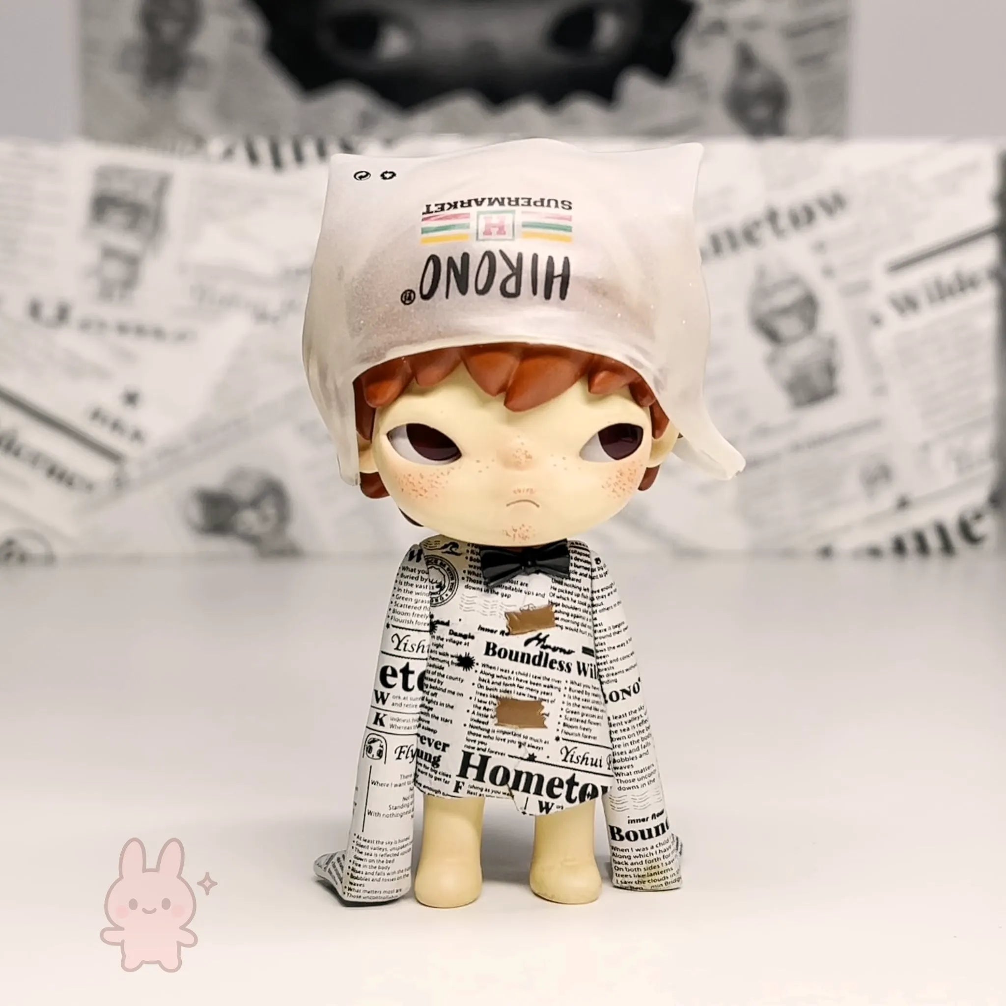 Pop Mart Hirono Little Mischief Toy figure wearing a newspaper outfit with a white cap on a light background