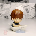 Pop Mart Hirono Little Mischief Small figurine of a boy with brown hair sitting in a paper boat on a light surface.