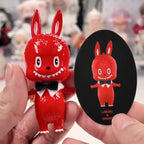 Pop Mart The Monsters 10th-anniversary Red character figurine held by a hand with a matching sticker in the background