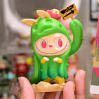 Pop Mart The Monsters Almost Hidden Colorful figurine with a green hood and pink cheeks held by a hand, with a blurred background.