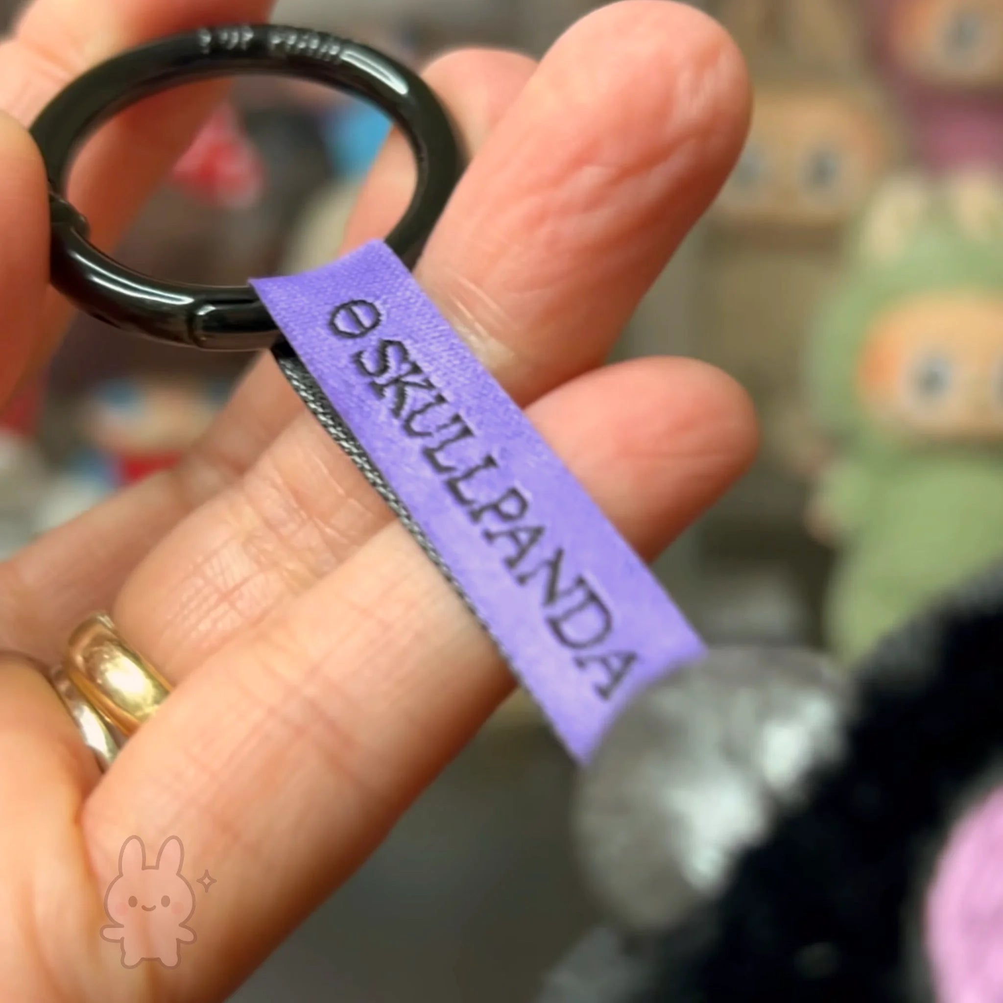 SKULLPANDA KUROMI Plush Keychain with purple tag labeled 'Skulpanda' held by a hand.