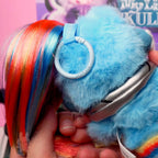 SKULLPANDA My Little Pony Plush Blue plush toy with colorful hair held by a hand against a blurred background