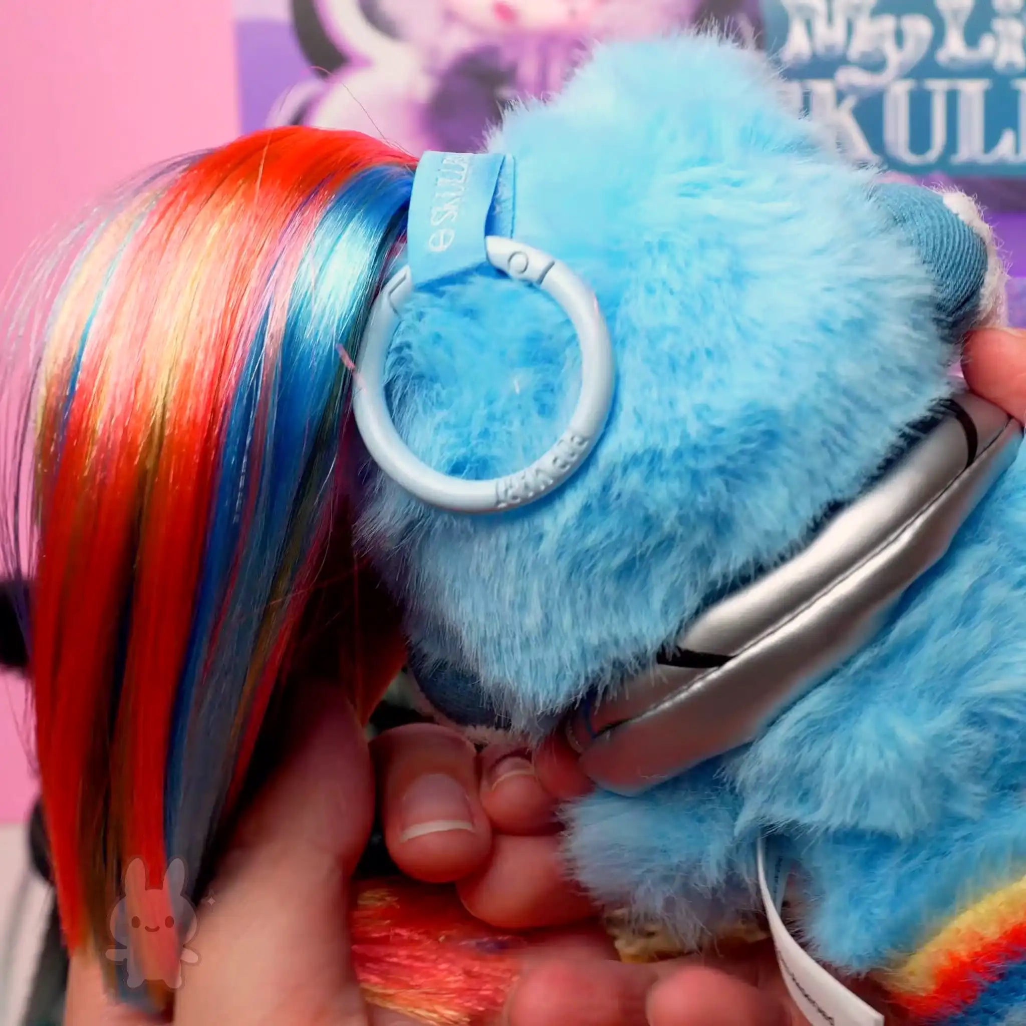 SKULLPANDA My Little Pony Plush Blue plush toy with colorful hair held by a hand against a blurred background