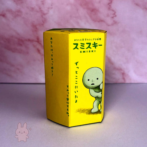 Yellow Smiski box with a cartoon character on a pink and gray background