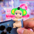 Sunny Angel Hippers Small figurine with green head and yellow ears held against a phone camera lens