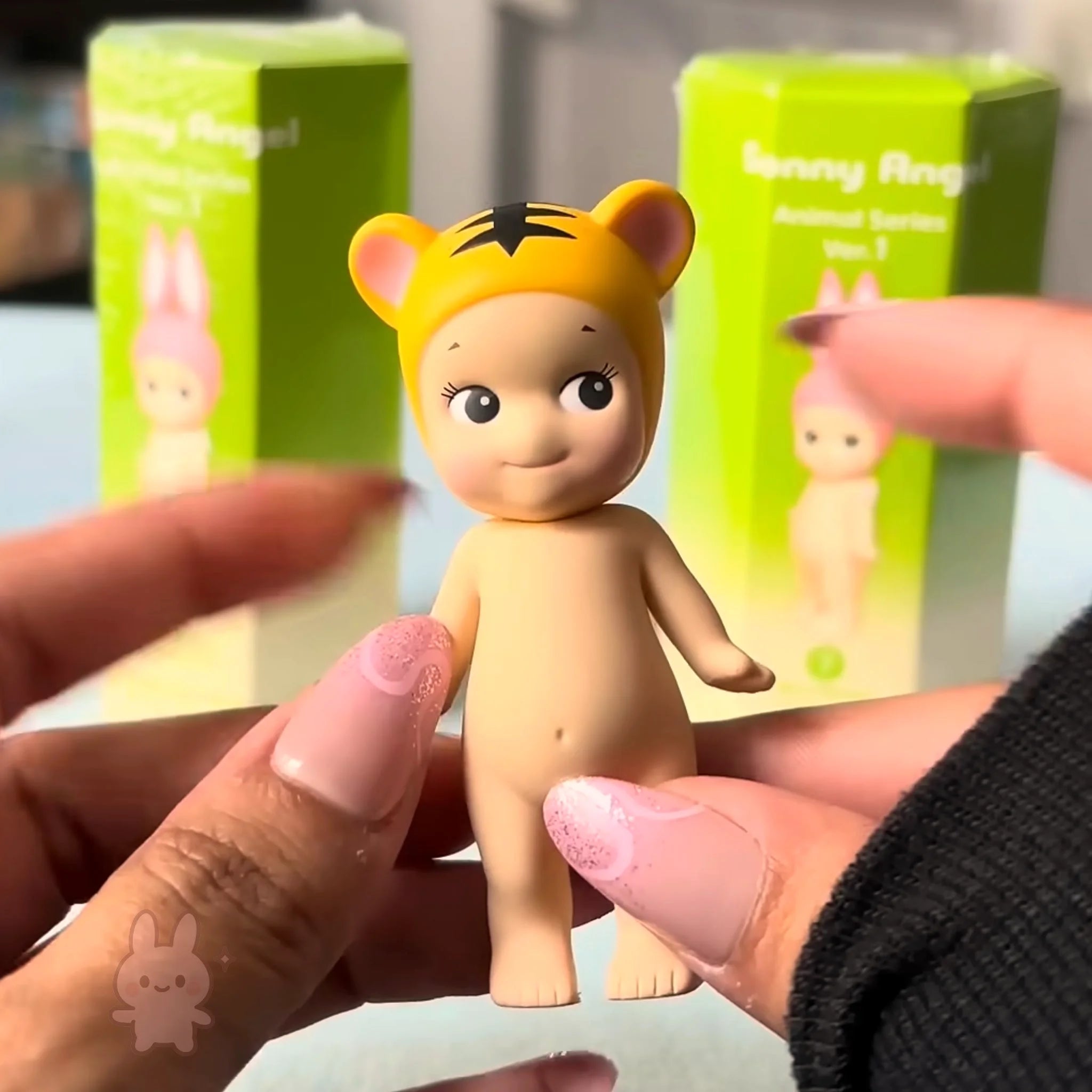 Sonny Angel Animal Series Ver.1 Toy figure with tiger hat held by hands, with green boxes in the background
