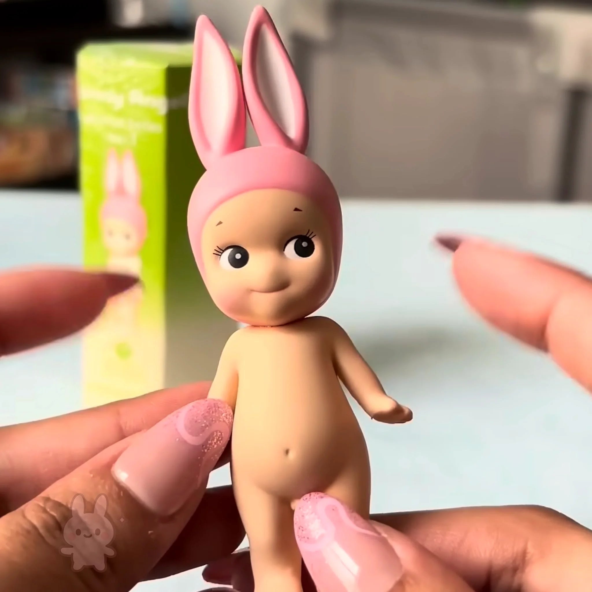 Sonny Angel Animal Series Ver.1 Toy figure with pink bunny ears held by hands against a blurred background