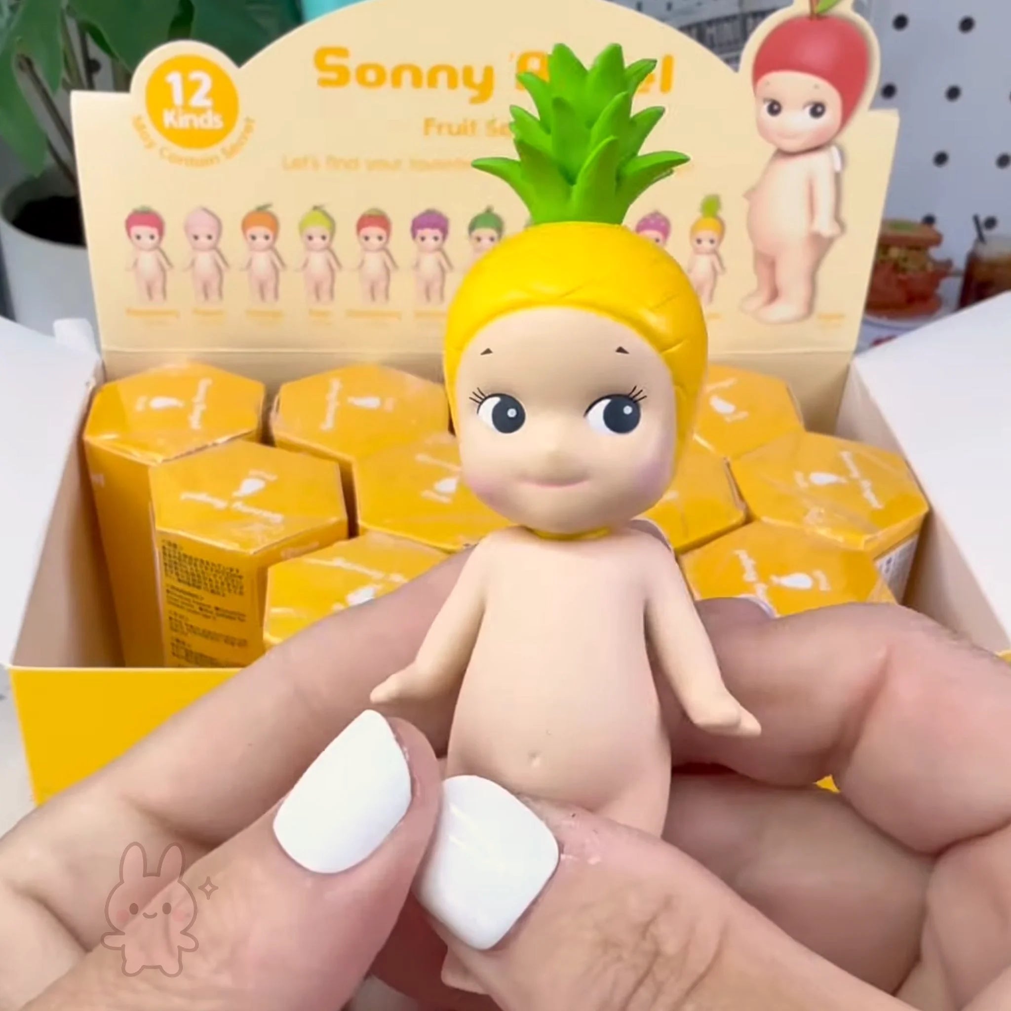 Sonny Angel fruit Toy figure with pineapple on head held by a hand, with packaging in the background