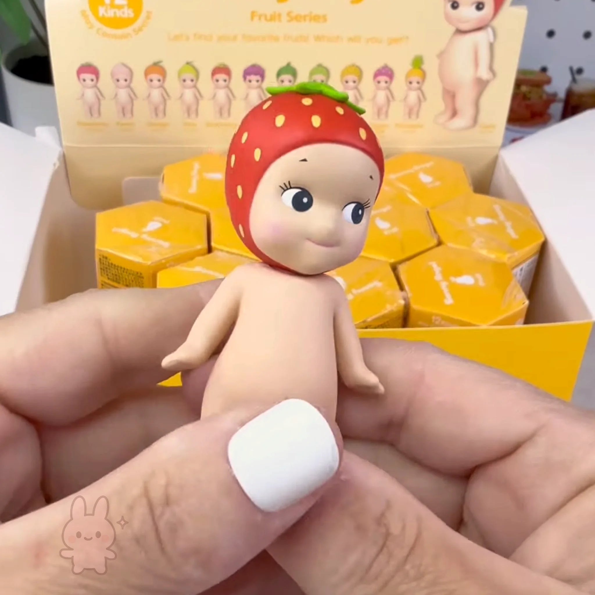 Sonny Angel fruit Toy figure with strawberry hat held by a hand, with packaging in the background