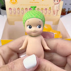Sonny Angel fruit Toy figure with a green hat held in hands, with packaging in the background