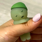 SMISKI Small green figurine held between fingers against a neutral background