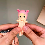 Sonny-Angel-hippers-animal Small figurine of a character in a pink outfit held between two hands against a neutral background.