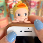 Sonny-Angel-hippers-animal Toy figure of a baby with a duck hat on top of a phone