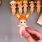 Sonny-Angel-hippers-animal Hand holding a small figurine with deer-like features against a gray background with other similar figurines.