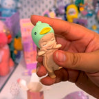 Sonny Angel hippers dreaming Hand holding a small figurine of a baby with a duck head against a colorful background