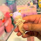 Sonny Angel hippers dreaming Hand holding a small figurine of a baby in a pink outfit with a blurred store background
