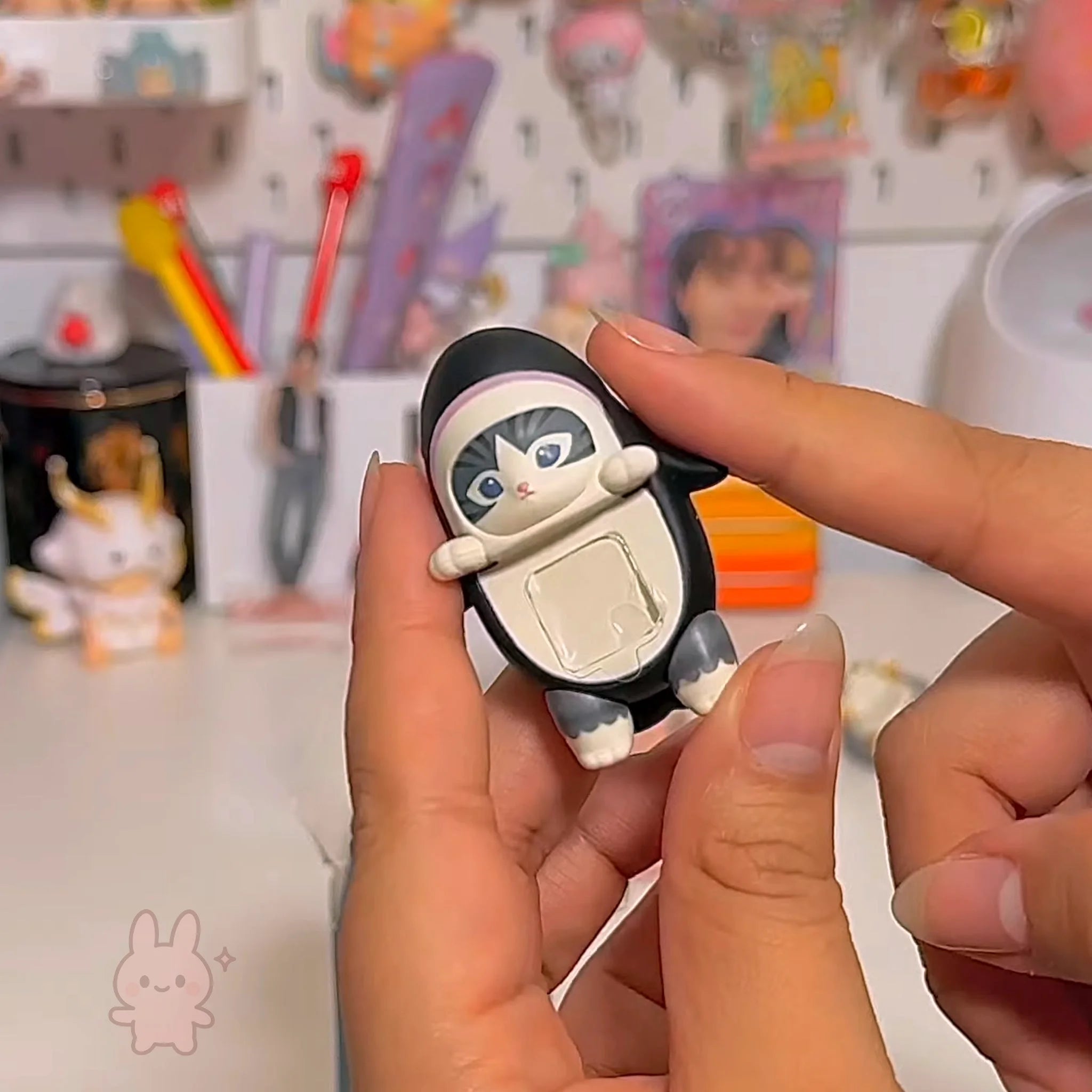 Sonny Angel Mofusand Hippers Person holding a small black and white figurine with a cat-like face against a colorful background.