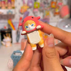 Sonny Angel Mofusand Hippers Small orange and white cat figurine with a red hat held by a hand against a colorful blurred background.