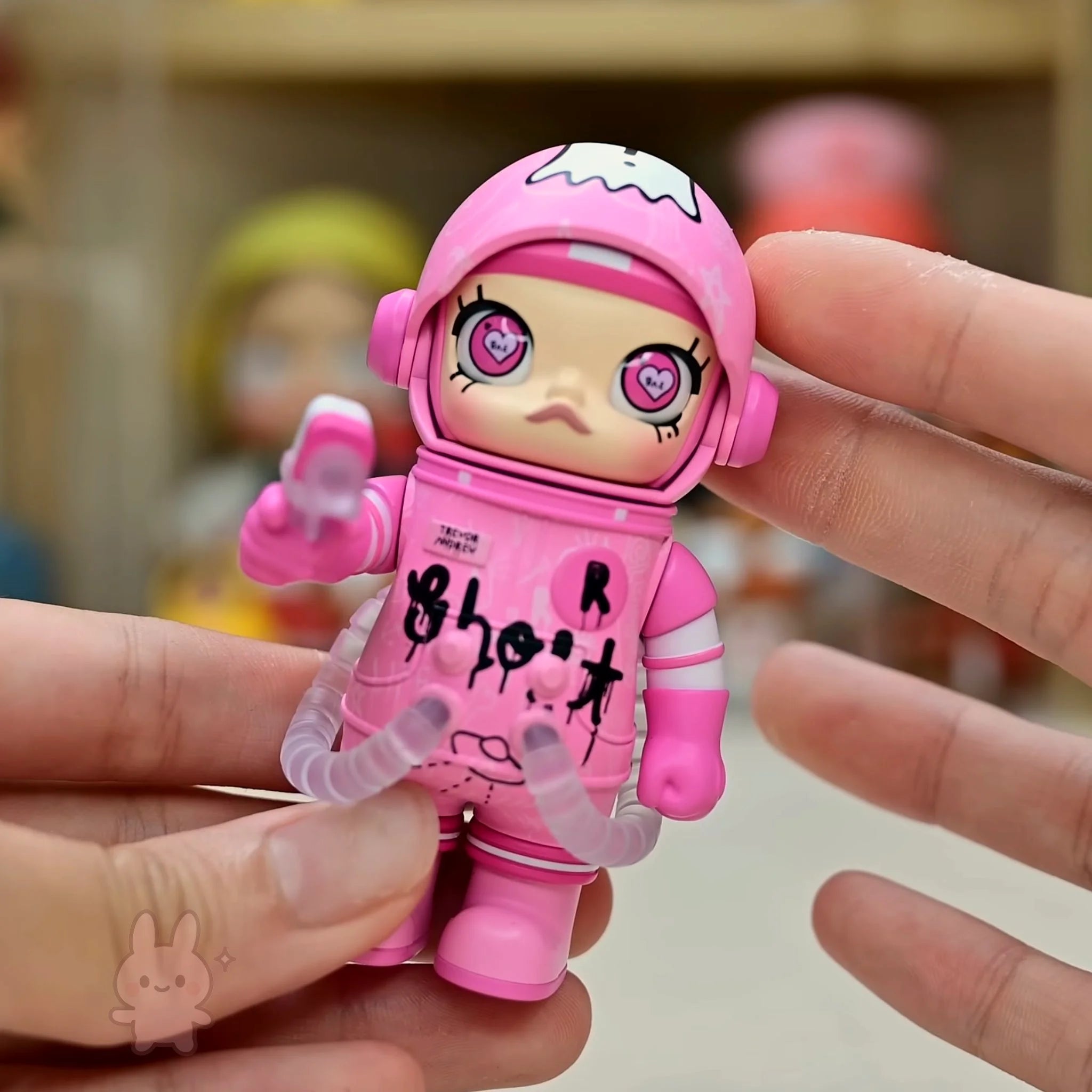 Space molly 100 series4 Pink toy figure with a stylized face held between two fingers against a blurred background