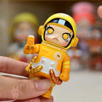 Space molly 100 series4 Toy figure in a yellow astronaut suit held by a hand with a blurred background