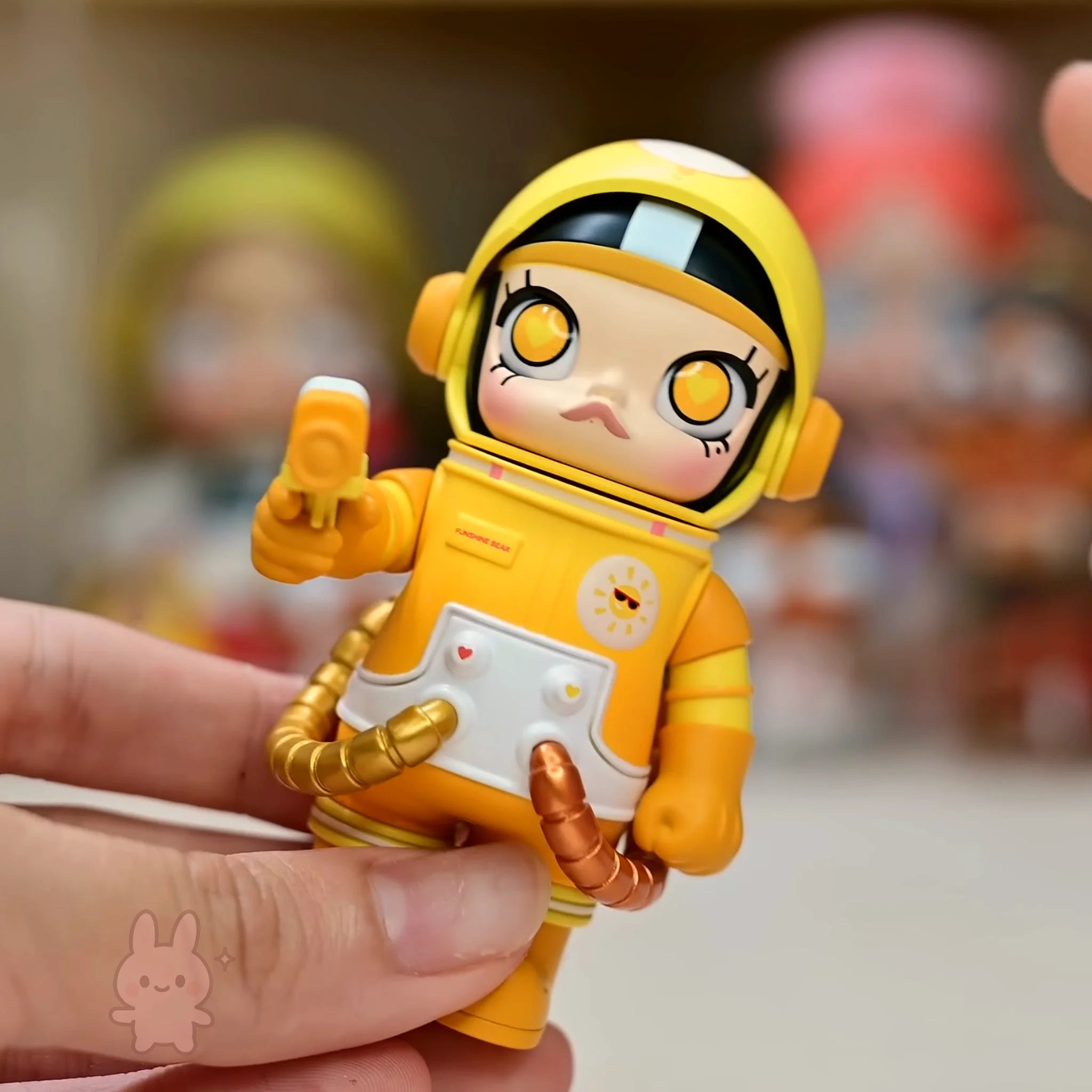 Space molly 100 series4 Toy figure in a yellow astronaut suit held by a hand with a blurred background