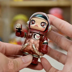 Space molly 100 series4 Small figurine of a character in a red suit with gold accents held by a hand.