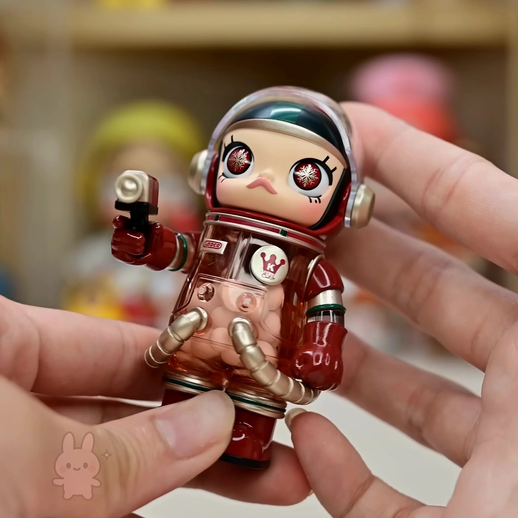 Space molly 100 series4 Small figurine of a character in a red suit with gold accents held by a hand.