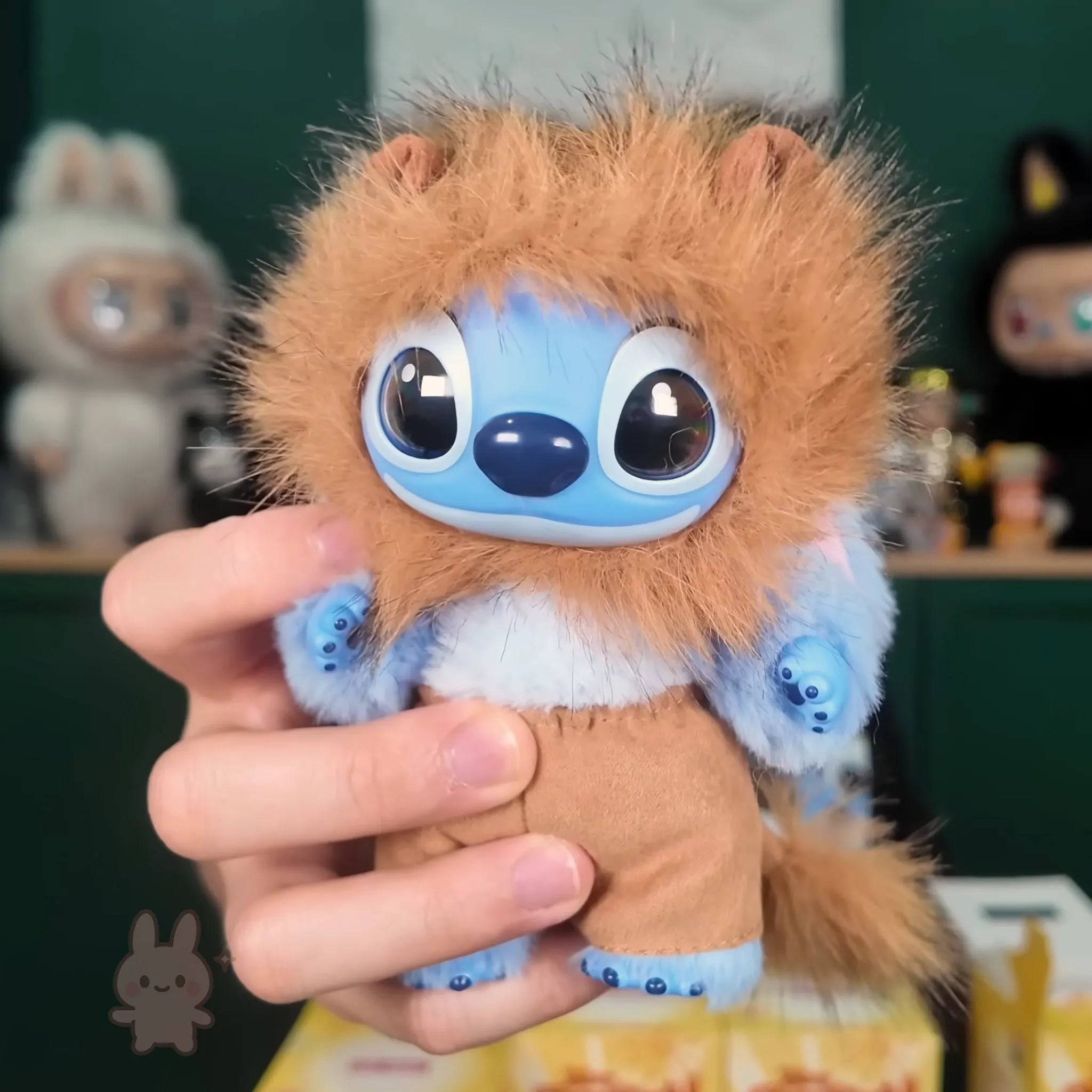 Stitch Adventure Plush toy resembling a character with large blue eyes and brown fur held by a hand against a blurred background.