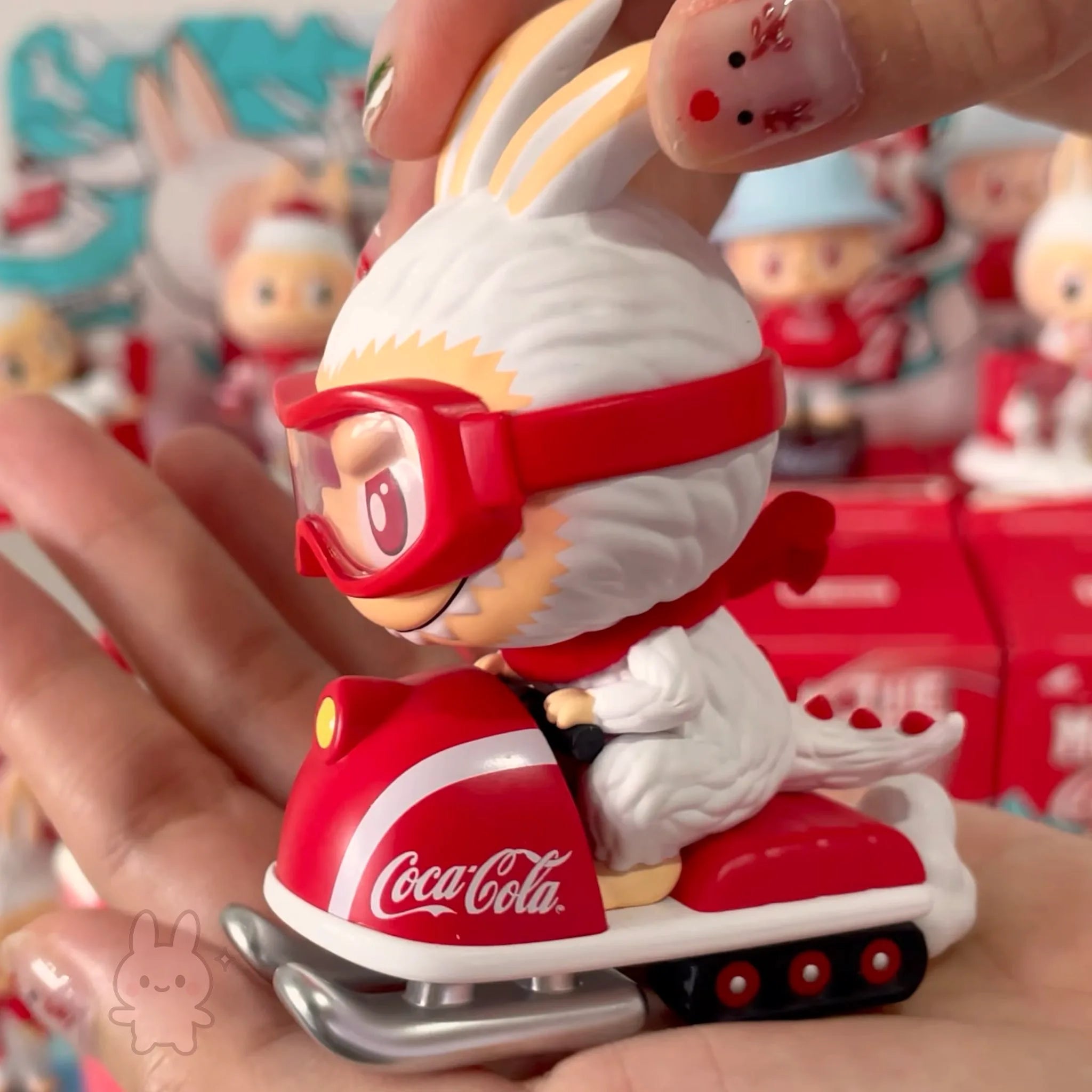 The Monsters Coca-Cola Toy figure of a character on a Coca-Cola scooter held in a hand with a blurred background of similar toys.